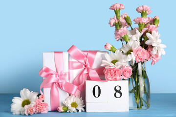 Cube calendar with date MARCH 8, beautiful flowers and gift boxes on blue wooden table. Women's Day celebration
