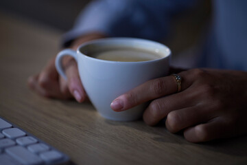 Woman hands, tea and night computer work of a female freelancer at home with hot drink. House, technology and cup with coffee or cappuccino by a desk with a young person doing remote working