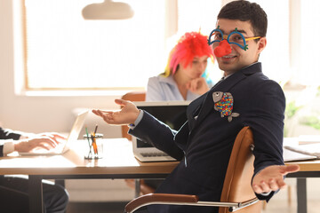 Obraz premium Young man with funny disguise working in office. April Fools' Day celebration