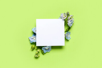 Composition with blank card and beautiful delphinium flowers on green background