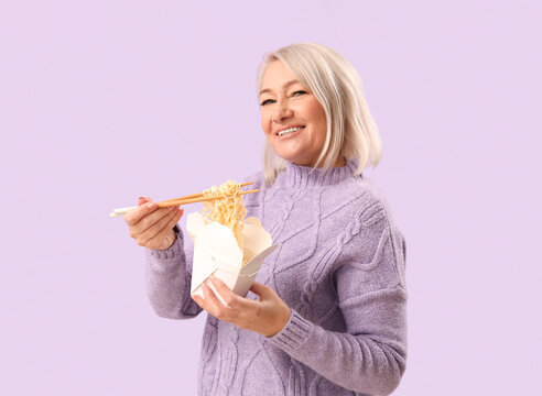 Mature woman holding container with tasty Chinese food on lilac background