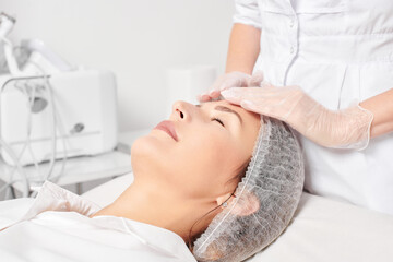 Cosmetologist massages woman face skin after rubbing moisturizing cream for rejuvenation, anti...