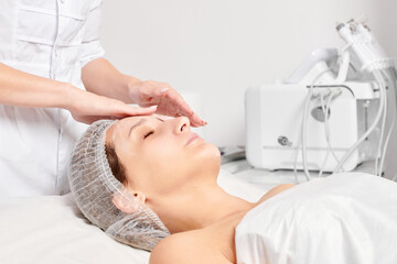Beautician rubbing moisturizing cream mask into woman face skin for rejuvenation, anti aging...