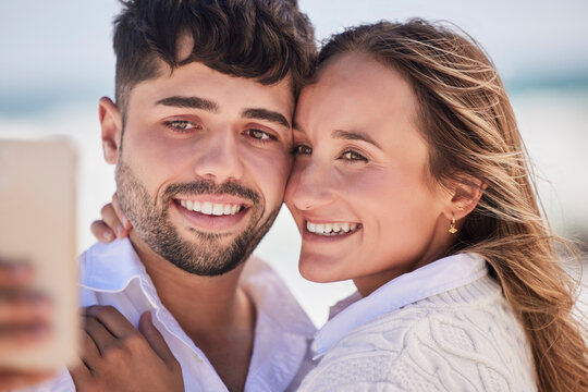 Selfie, love and couple on a date at the beach for valentines day, romance or anniversary in summer. Happiness, smile and young man and woman hugging while taking picture by the ocean on vacation.