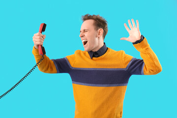 Screaming young man with phone receiver on blue background