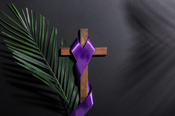 Cross with purple ribbon and palm leaf on dark background. Good Friday concept
