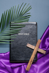 Holy Bible with cross, palm leaf and purple fabric on blue background. Good Friday concept