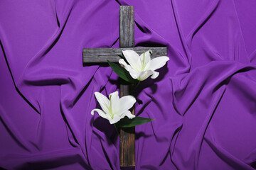 Wooden cross with lily flowers on purple fabric background. Good Friday concept