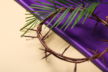Crown of thorns with palm leaf and purple fabric on beige background, closeup. Good Friday concept