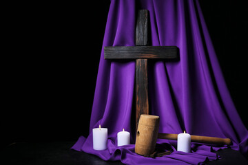 Cross with hammer, burning candles and purple fabric on dark background. Good Friday concept