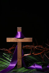 Cross with purple ribbon, crown of thorns and palm leaf on dark background. Good Friday concept