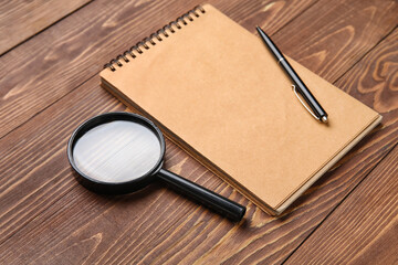 Blank notebook, magnifier and pen on wooden background. World Poetry Day celebration