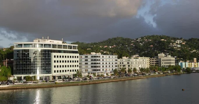 Traffic flowing on John Compton Hwy paralleling the shoreline of Castries Harbor, St. Lucia as the late afternoon sun lights buildings with a warm glow.