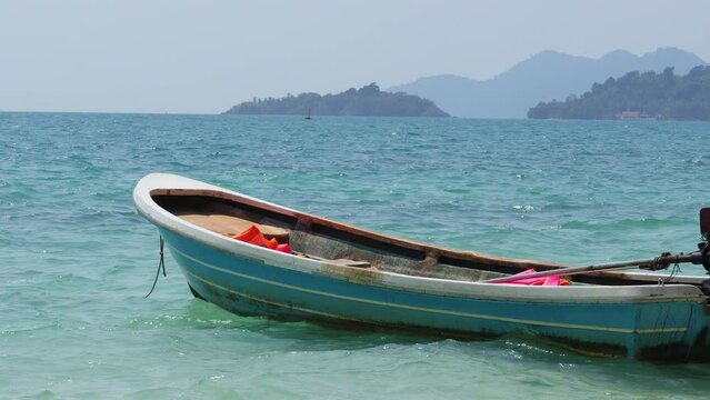 Beautiful scenery and blue boat on a beach with sea waves at Koh Chang, Thailand.Clear water of sea waves on the beautiful beach. Scenic relaxing scenery