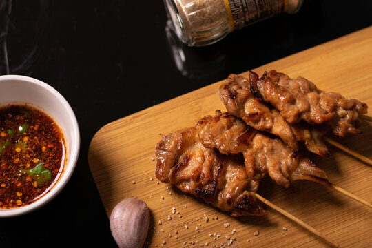 Grilled pork (mooping) and spicy sauce on a wooden chopping board, decorated with garlic and roasted rice