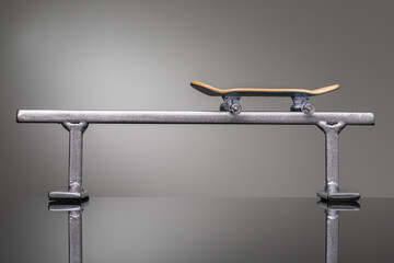 Children's fingerboard on a metal railing on a gray gradient background, a small skateboard