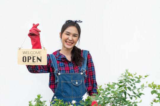 Portrait of Beautiful Asian woman gardener holding a open sign board in white background. Young entrepreneur working in botanical nursery garden. Sustainability in small business owner