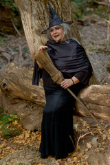 white-haired witch sitting on the river bank with her broomstick