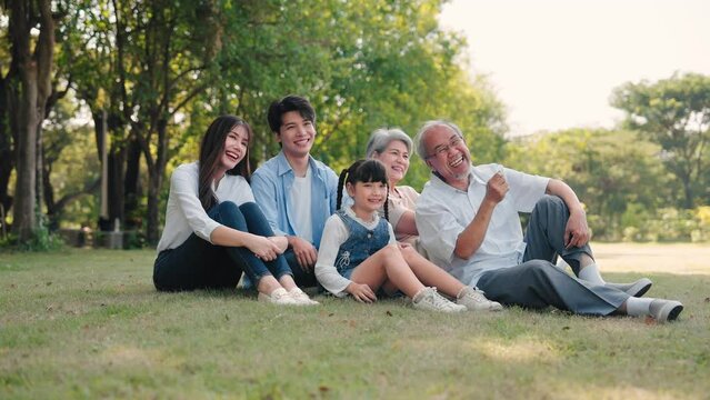 Asian family talking and sitting on grass in a park during summer morning