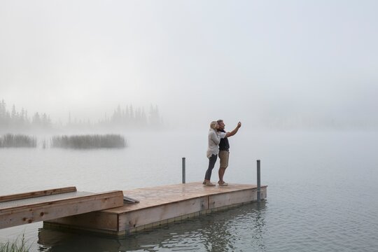 Couple take selfie pic across mountain lake, fog