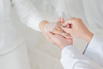 malay wedding groom bolstering ring on bride's finger. Groom wear wedding rings to left finger of...