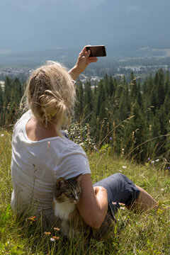 Woman takes photo with cat in mountain meadow