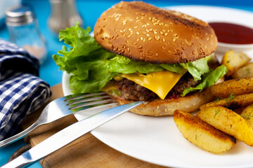 Homemade imperfect burger with potatoes and salad on a plate. Food on the table in a white plate on a wooden board