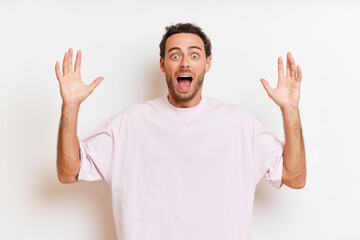 Indoor shot of stunned European man keeps palms raised exclaims with surprise can not believe own eyes wears bright t-shirt poses over white wall