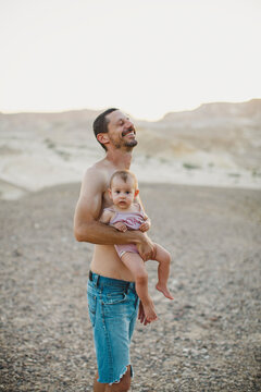 A father laughing while holding his baby girl in the desert