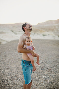 A father laughing while holding his baby girl in the desert