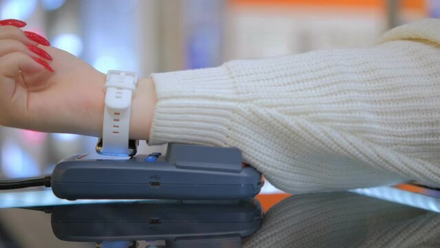 Wireless payment by smart watch using e wallet on pos terminal or card reader. Female buyer hand pays electronic cashless money at shopping place close up indoors