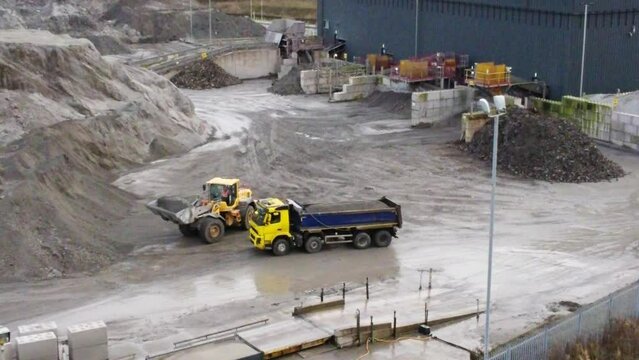 Aerial view orbiting bulldozer loading quarry material onto truck reversing on power station coal site