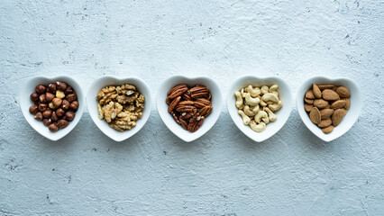Top view, close up, on a textured white concrete background, five heart shaped bowls with shelled mixed nuts - 572582697