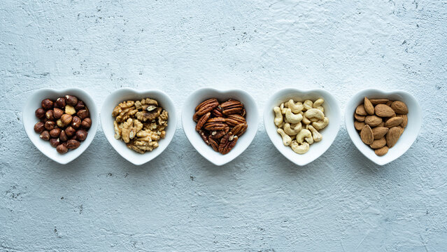 Top view, close up, on a textured white concrete background, five heart shaped bowls with shelled mixed nuts