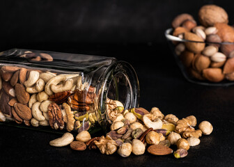 on a dark textured background, a clear glass jar with shelled mixed dried fruits. Copy space. - 572583244
