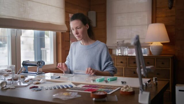 young woman makes handmade earrings of polymer clay sitting at table at home. self taught artist creates craft jewellery