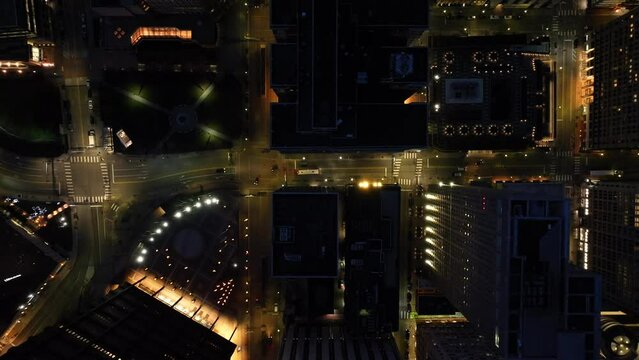 Top Down Aerial Shot Of Large American City At Night. Light Traffic And City Bus Driving On Streets Below. High Drone Shot At Dusk.