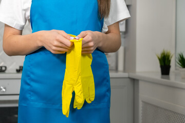 Close-up of women's hands holding yellow rubber gloves. Woman in uniform is preparing to clean the apartment, copy space