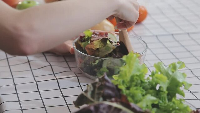 Young and happy woman eating healthy salad sitting on the table with green fresh ingredients indoors