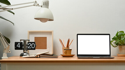 Bright home office interior with laptop computer, picture frame, potted plant and picture frame on...