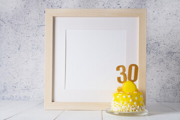 The number Thirty on the yellow cake next to the white frame mockup with copy space.