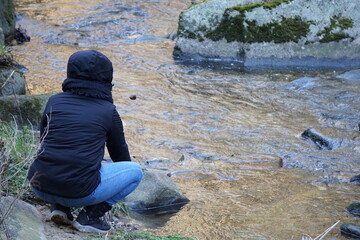 Kobieta kuca nad potokiem i patrzy przed siebie