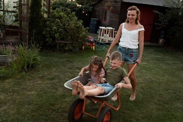 Young mother plays with children and garden cart at dackyard