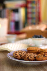 Plate of cookies, cup of tea, fresh blueberries, dry oranges, stack of books, reading glasses and tablet on the table. Hygge at home. Selective focus.