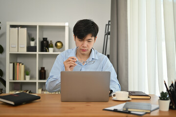 Focused man manager looking at laptop watching online webinar training or having virtual meeting video conference in office