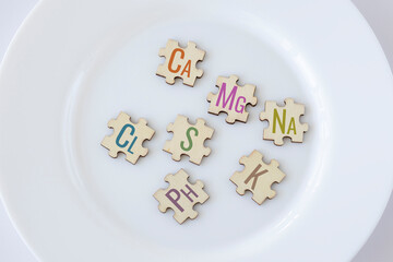 Set of puzzles on a plate with 7 essential Macronutrients with colorful icon lettering. Ca, Mg, Na, Cl, S, Ph, S, K. Biologically important elements. The concept of healthy nutrition and health