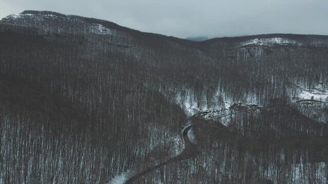 Aerial view of a serpentine road crossing a forest in wintertime with snow on Mount Terminio, Serino, Avellino, Irpinia, Campania, Italy.