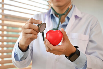 Doctor in white uniform holding stethoscope and red heart shape. Health care, organ donation and...