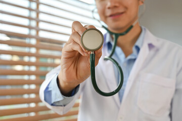 Cropped image of smiling male doctor in white uniform holding stethoscope. Healthcare and medical concept