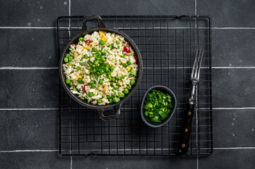 Asian Fried rice with egg and vegetables in a skillet. Black background. Top view